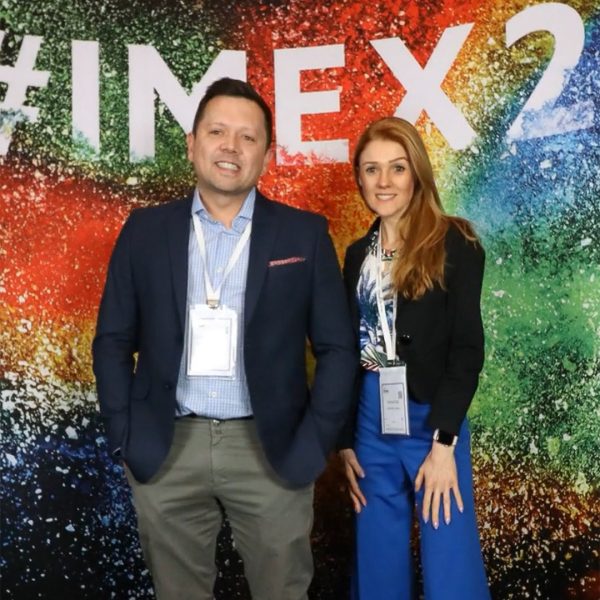 Fernando Dellazzari e Marina Poli em frente ao painel colorido com marca IMEX America